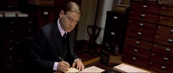 Movie still from “Rabbit-Proof Fence” (2002), directed by Phillip Noyce – A man sitting at a desk writing on a piece of paper; Medium shot, Low angle
