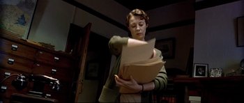 Movie still from “Rabbit-Proof Fence” (2002), directed by Phillip Noyce – A woman holding a stack of papers in a cluttered room; Medium shot, Low angle
