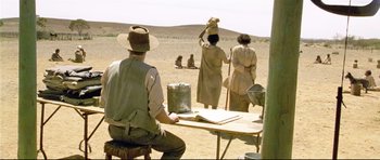 Movie still from “Rabbit-Proof Fence” (2002), directed by Phillip Noyce – A group of people standing around a table in the desert; Wide shot, Over the shoulder angle