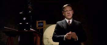 Movie still from “Rabbit-Proof Fence” (2002), directed by Phillip Noyce – A man wearing a suit and tie standing in front of a camera; Medium shot, Low angle