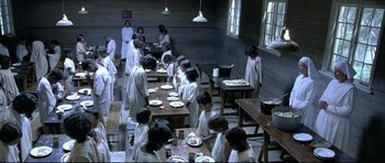 Movie still from “Rabbit-Proof Fence” (2002), directed by Phillip Noyce – A group of people sitting around a table with plates on top of it; Wide shot, High angle
