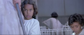 Movie still from “Rabbit-Proof Fence” (2002), directed by Phillip Noyce – A young girl in a white shirt is standing in front of a white fence; Close Up shot, Over the shoulder angle