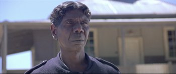 Movie still from “Rabbit-Proof Fence” (2002), directed by Phillip Noyce – An older man with a black shirt and a black jacket; Close Up shot, Over the shoulder angle