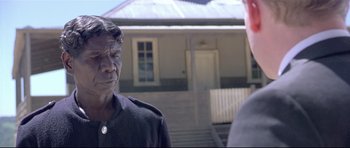 Movie still from “Rabbit-Proof Fence” (2002), directed by Phillip Noyce – A man standing next to another man in front of a house; Close Up shot, Over the shoulder angle