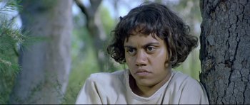 Movie still from “Rabbit-Proof Fence” (2002), directed by Phillip Noyce – A young man with a black hair is looking at the camera; Close Up shot, High angle