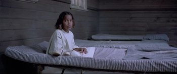 Movie still from “Rabbit-Proof Fence” (2002), directed by Phillip Noyce – A young girl sitting on top of a bed in a room; Close Up shot, High angle