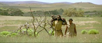 Movie still from “Rabbit-Proof Fence” (2002), directed by Phillip Noyce – A man holding two monkeys in a field; Wide shot, Low angle