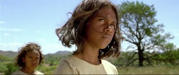 Movie still from “Rabbit-Proof Fence” (2002), directed by Phillip Noyce – A young girl with long hair is standing in a field; Close Up shot, Low angle