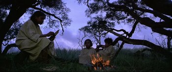 Movie still from “Rabbit-Proof Fence” (2002), directed by Phillip Noyce – A group of people sitting around a fire in the woods; Wide shot, Low angle