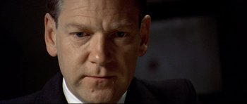 Movie still from “Rabbit-Proof Fence” (2002), directed by Phillip Noyce – A man in a suit and tie looking at the camera; Close Up shot, High angle