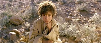 Movie still from “Rabbit-Proof Fence” (2002), directed by Phillip Noyce – A young boy sitting on the ground in the desert; Close Up shot, High angle