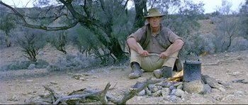Movie still from “Rabbit-Proof Fence” (2002), directed by Phillip Noyce – A man sitting on the ground next to a fire pit; Wide shot, Low angle