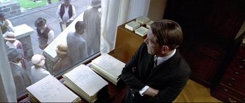 Movie still from “Rabbit-Proof Fence” (2002), directed by Phillip Noyce – A man sitting at a table with a bunch of papers; Medium shot, Over the shoulder angle