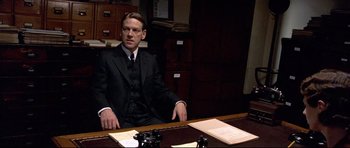 Movie still from “Rabbit-Proof Fence” (2002), directed by Phillip Noyce – A man sitting at a desk in a suit and tie; Medium shot, High angle