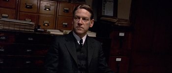 Movie still from “Rabbit-Proof Fence” (2002), directed by Phillip Noyce – A man in a suit and tie sitting in front of a stack of papers; Close Up shot, Low angle