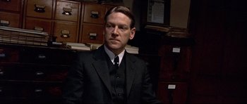 Movie still from “Rabbit-Proof Fence” (2002), directed by Phillip Noyce – A man in a suit and tie sitting in front of a pile of papers; Close Up shot, Low angle