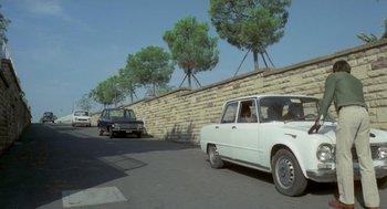 Movie still from “Rabid Dogs” (1974), directed by Mario Bava – A couple of cars parked next to each other on the side of the road; Extreme Wide shot, Low angle