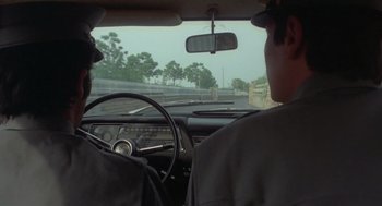 Movie still from “Rabid Dogs” (1974), directed by Mario Bava – Two men in the drivers seat of an old car; Medium shot, Low angle