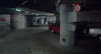 Movie still from “Rabid Dogs” (1974), directed by Mario Bava – A red car parked in a parking garage next to a sign; Extreme Wide shot, High angle