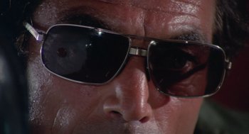 Movie still from “Rabid Dogs” (1974), directed by Mario Bava – A man's face wearing a pair of sunglasses; Extreme Close Up shot, Low angle