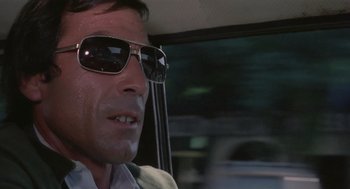 Movie still from “Rabid Dogs” (1974), directed by Mario Bava – A person wearing sunglasses driving a car; Close Up shot, Low angle