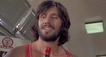 Movie still from “Rabid Dogs” (1974), directed by Mario Bava – A man with long hair and beard holding a bottle of beer; Close Up shot, Low angle