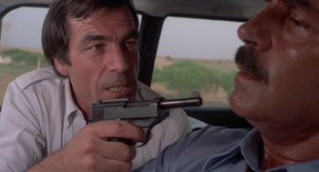 Movie still from “Rabid Dogs” (1974), directed by Mario Bava – A man holding a gun pointed at another man in the back of a car; Close Up shot, Over the shoulder angle