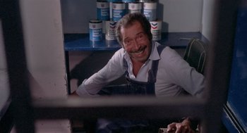 Movie still from “Rabid Dogs” (1974), directed by Mario Bava – An older man sitting in front of a shelf of paint; Medium shot, High angle