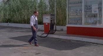 Movie still from “Rabid Dogs” (1974), directed by Mario Bava – A man walking down the street next to a gas pump; Wide shot, High angle