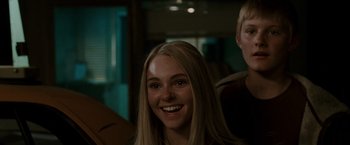 Movie still from “Race to Witch Mountain” (2009), directed by Andy Fickman – A woman smiles brightly at the camera while a man looks on; Close Up shot, Over the shoulder angle