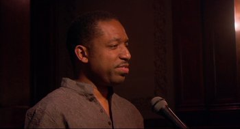 Movie still from “Rachel Getting Married” (2008), directed by Jonathan Demme – A man is speaking into a microphone in front of a wall; Close Up shot, Low angle
