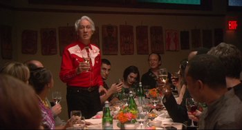 Movie still from “Rachel Getting Married” (2008), directed by Jonathan Demme – An older man standing at a dinner table with people; Medium shot, Over the shoulder angle
