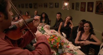 Movie still from “Rachel Getting Married” (2008), directed by Jonathan Demme – A group of people sitting at a table with a violin; Medium shot, High angle