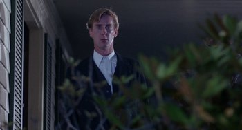 Movie still from “Rachel, Rachel” (1968), directed by Paul Newman – A man wearing a suit and tie standing next to a bush; Medium shot, Low angle