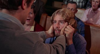 Movie still from “Rachel, Rachel” (1968), directed by Paul Newman – A man with long hair and a goateed face is holding his hands up to his face; Close Up shot, Over the shoulder angle