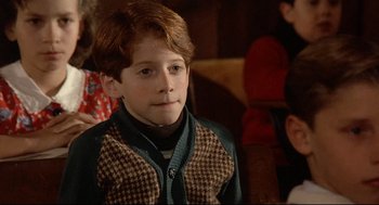 Movie still from “Radio Days” (1987), directed by Woody Allen – A young boy wearing a sweater and standing in front of a group of people; Close Up shot, High angle