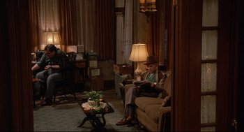 Movie still from “Radio Days” (1987), directed by Woody Allen – An older man sitting on a couch in a living room; Wide shot, High angle