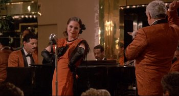 Movie still from “Radio Days” (1987), directed by Woody Allen – A woman in an orange dress holding a microphone; Medium shot, Over the shoulder angle