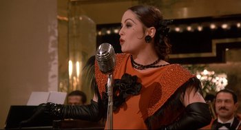 Movie still from “Radio Days” (1987), directed by Woody Allen – A woman in an orange and black dress talking into a microphone; Close Up shot, Low angle