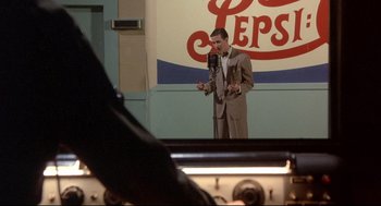 Movie still from “Radio Days” (1987), directed by Woody Allen – A man standing in front of a microphone in front of a pepsi sign; Medium shot, Low angle