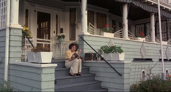 Movie still from “Radio Days” (1987), directed by Woody Allen – A woman sitting on the steps of a house giving a thumbs up; Wide shot, Low angle