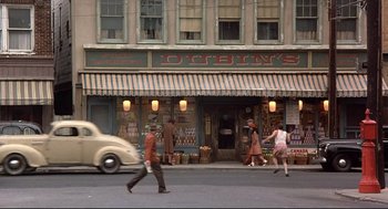 Movie still from “Radio Days” (1987), directed by Woody Allen – A group of people walking across a street near a building; Wide shot, High angle