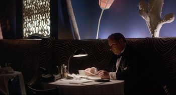 Movie still from “Radio Days” (1987), directed by Woody Allen – A man sitting at a table in front of papers; Medium shot, Low angle