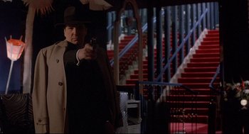 Movie still from “Radio Days” (1987), directed by Woody Allen – A man holding a gun while standing in front of stairs; Medium shot, Low angle