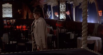 Movie still from “Radio Days” (1987), directed by Woody Allen – An older man in a hat and glasses standing in front of a bar; Wide shot, Over the shoulder angle
