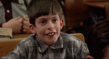 Movie still from “Radio Days” (1987), directed by Woody Allen – A young boy smiling for the camera while sitting in a chair; Close Up shot, Low angle