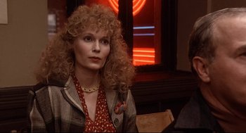 Movie still from “Radio Days” (1987), directed by Woody Allen – A woman with blonde curly hair sitting in front of a neon sign; Close Up shot, Over the shoulder angle