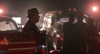 Movie still from “Radio Days” (1987), directed by Woody Allen – A man smoking a cigarette while standing next to a car; Medium shot, Over the shoulder angle