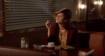 Movie still from “Radio Days” (1987), directed by Woody Allen – A woman sitting at a table smoking a cigarette; Medium shot, Low angle