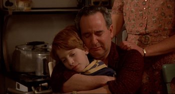 Movie still from “Radio Days” (1987), directed by Woody Allen – A man and a boy are hugging in a kitchen; Medium shot, High angle